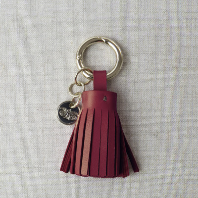Key holder and bag charms TASSEL in lambskin, bordeaux color and gold - front view on linen background